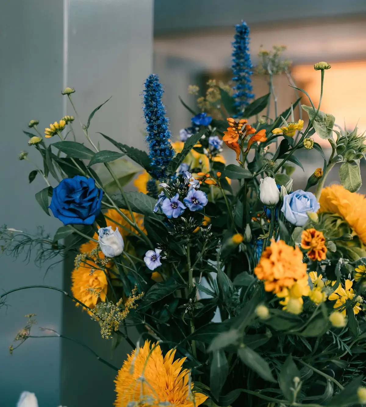 Een veldbloemenboeket in blauw, oranje en geel in warm avondlicht.