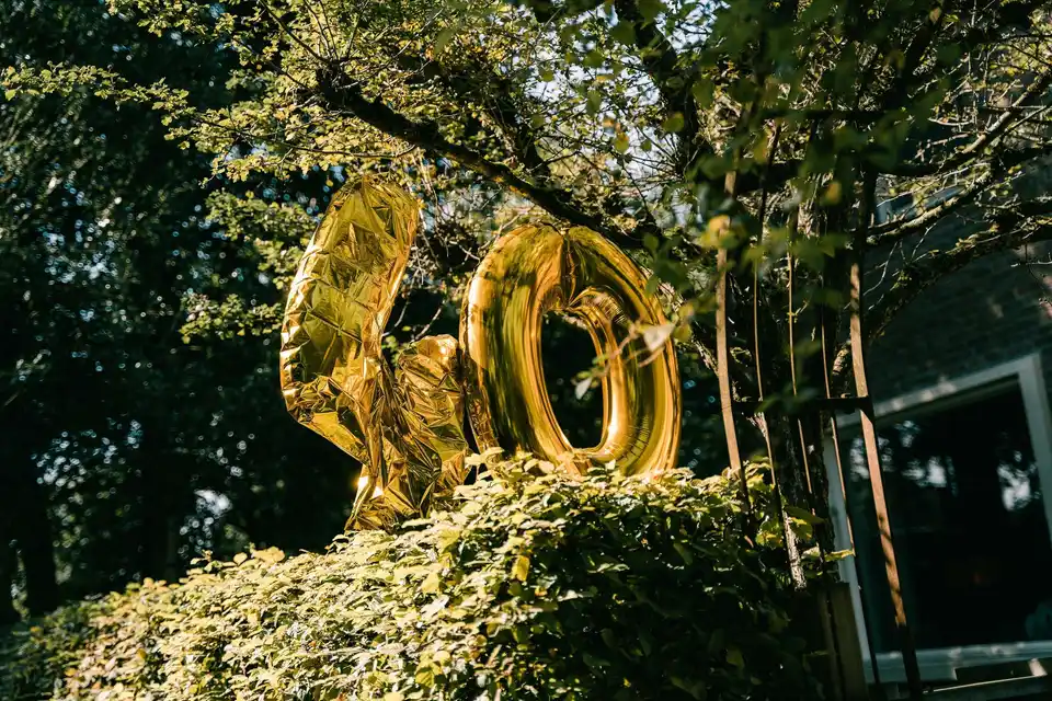 Gouden ballonnen in de vorm van een 40 tegen een groene haag in de tuin.