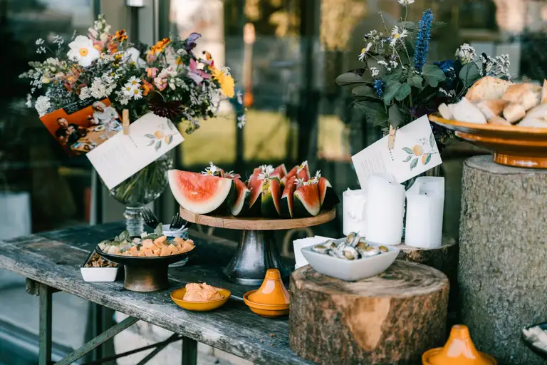 Buffet op een oude bank met veldbloemen, watermeloen, servies en menukaartjes.