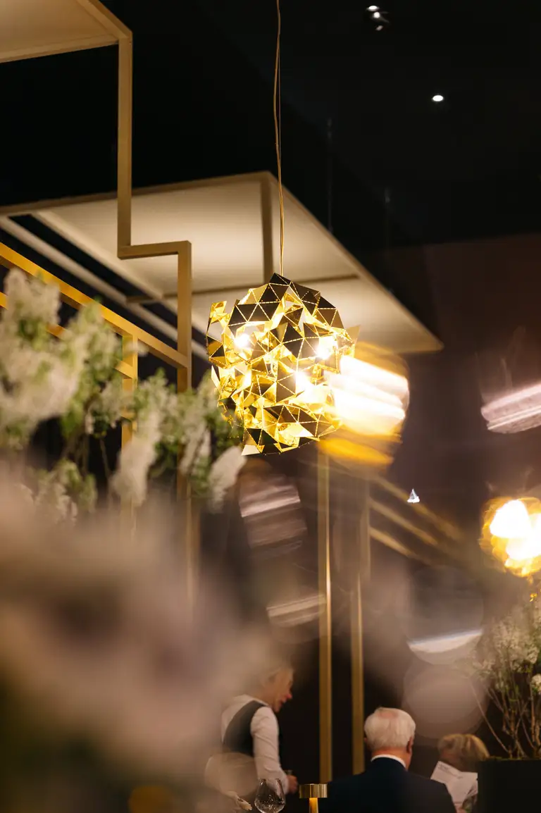 Een gouden lamp met witte bloemen in diepe bokeh in een warm verlichte zaal.